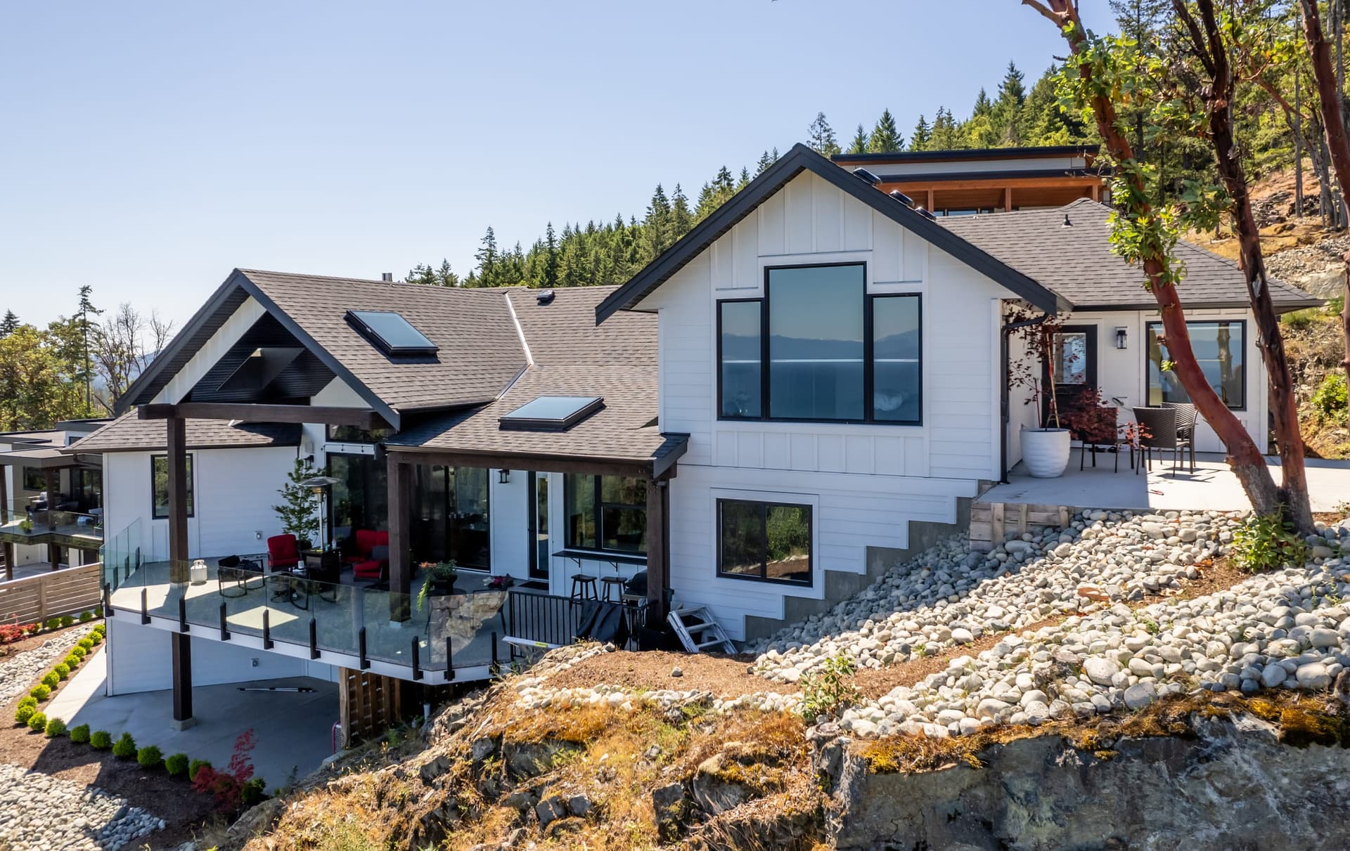 White Hardie board and batten home on a rocky hillside with glass deck railings and ocean views