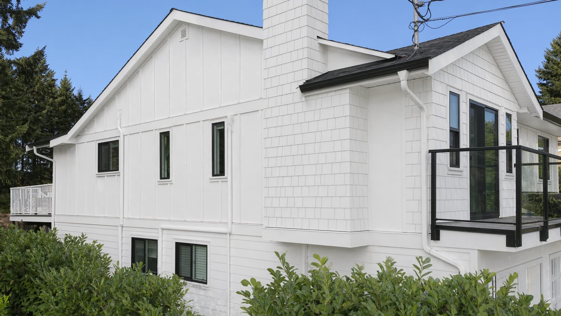 White Hardie board and batten and shingle siding with black windows and a glass-railed deck